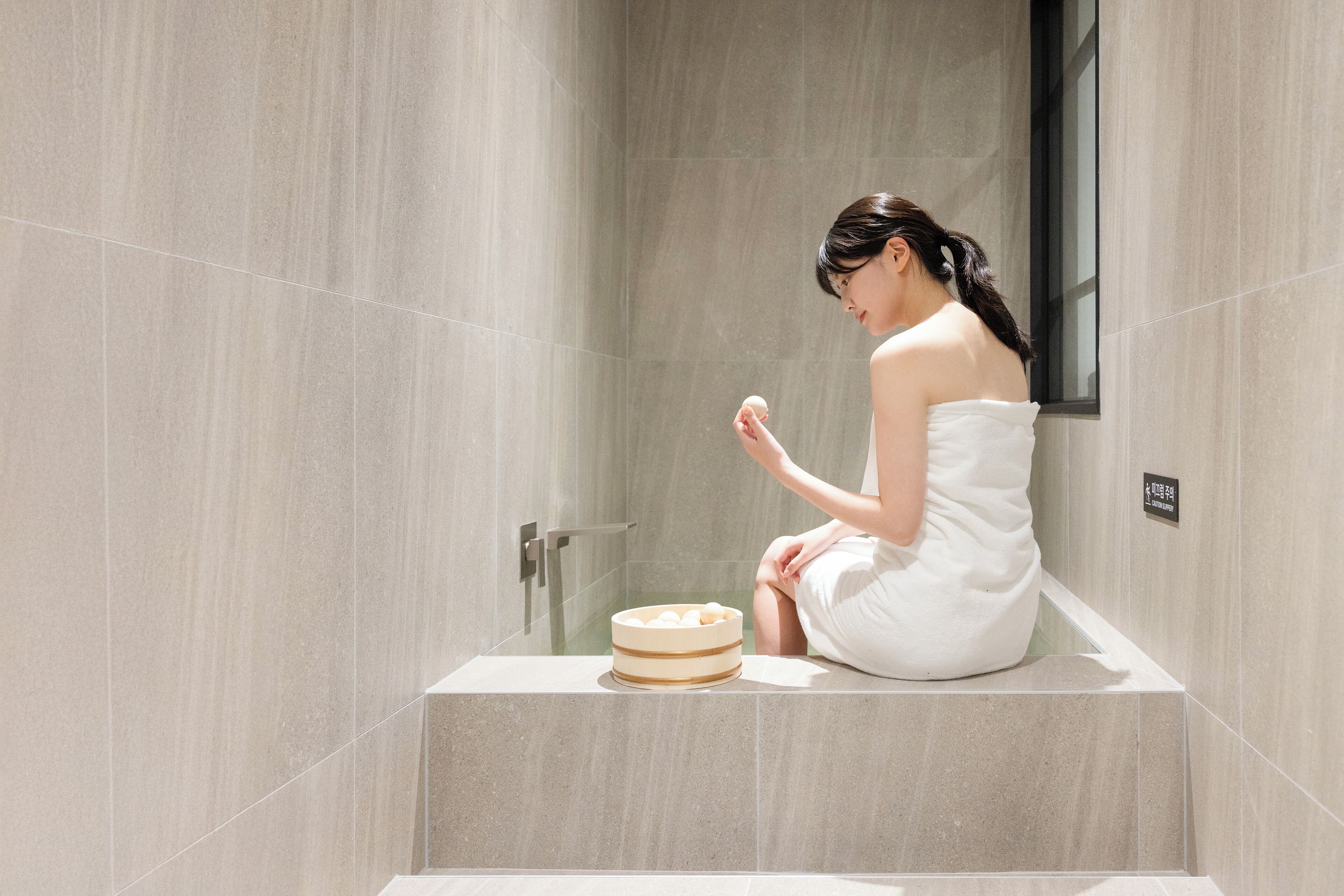 A person sitting on a bathtub in a bathroom with a towel wrapped around their body.