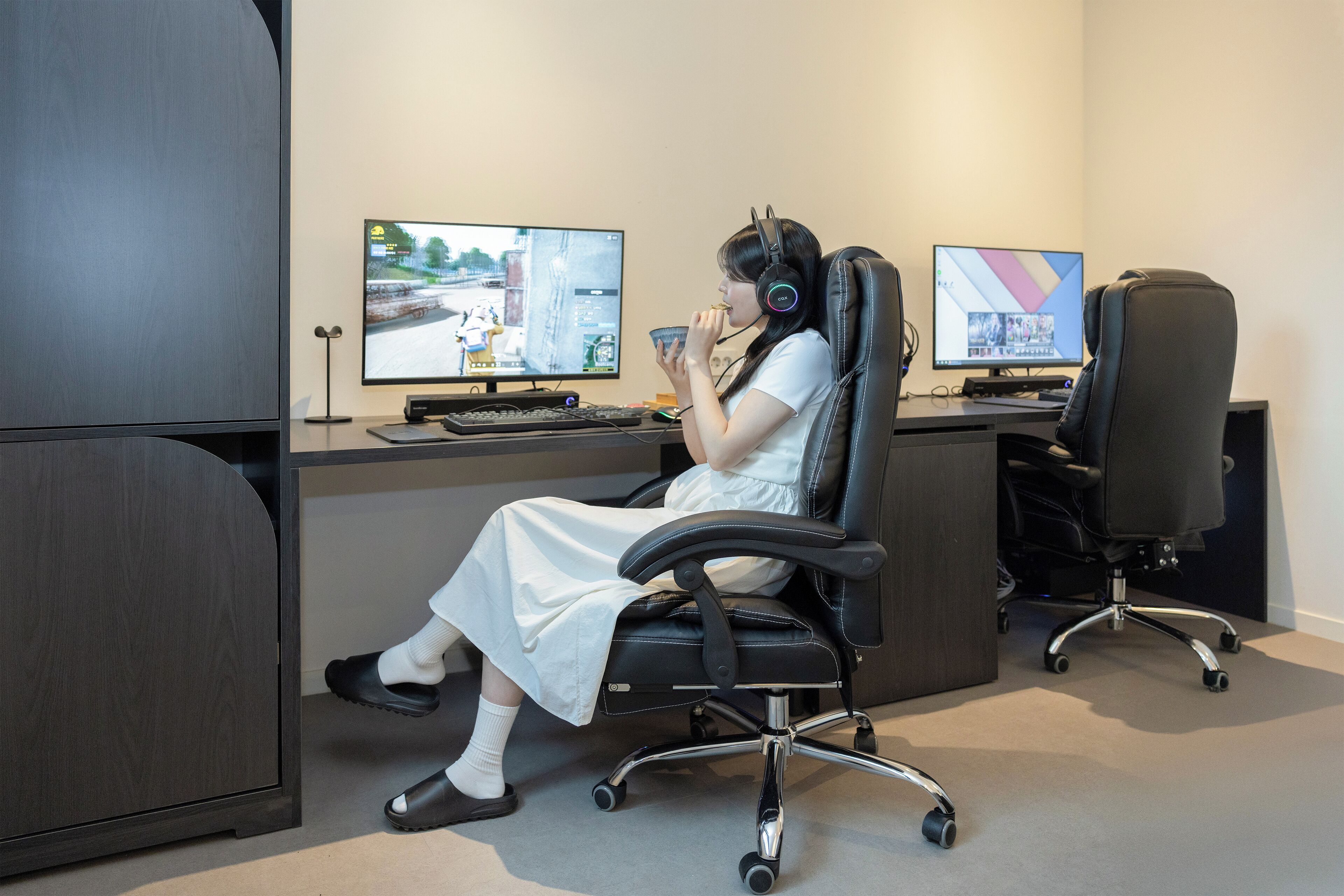A person seated at a desk with two monitors, a keyboard, and headphones.