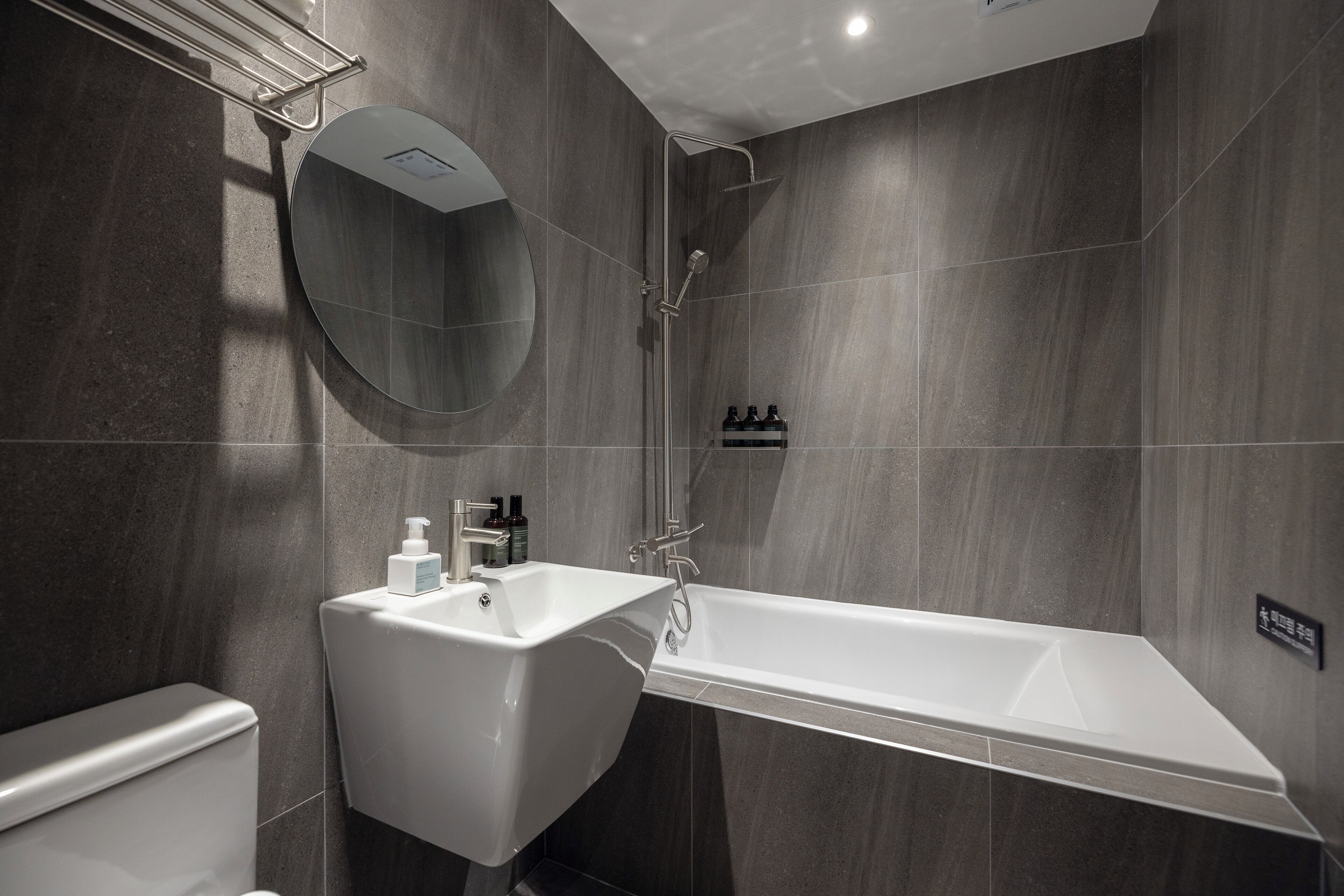 A modern bathroom with a white bathtub, a round mirror, and a toilet.