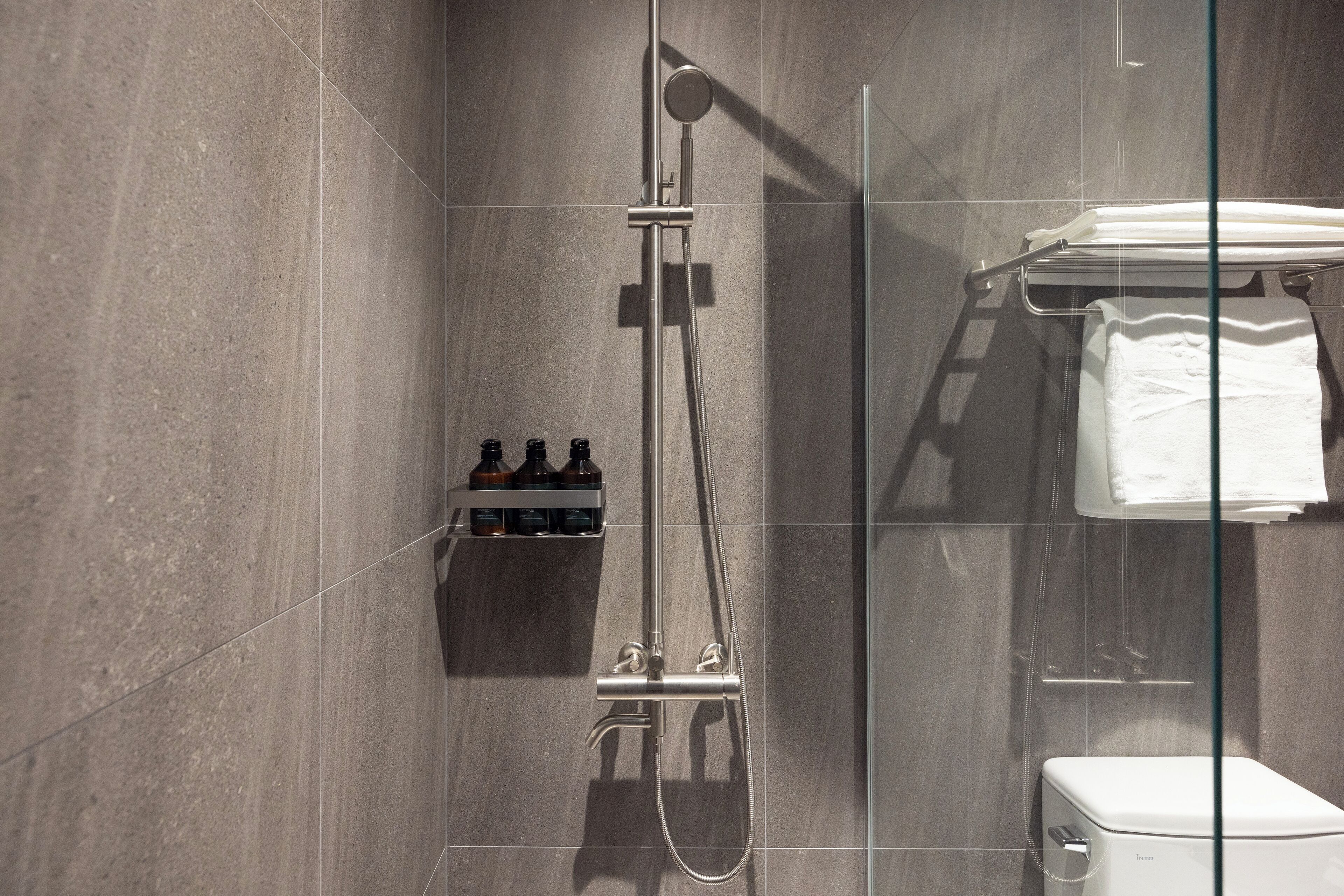 Ein modernes Badezimmer mit Duschkabine aus Glas, Toilette und Ablage für Toilettenartikel.