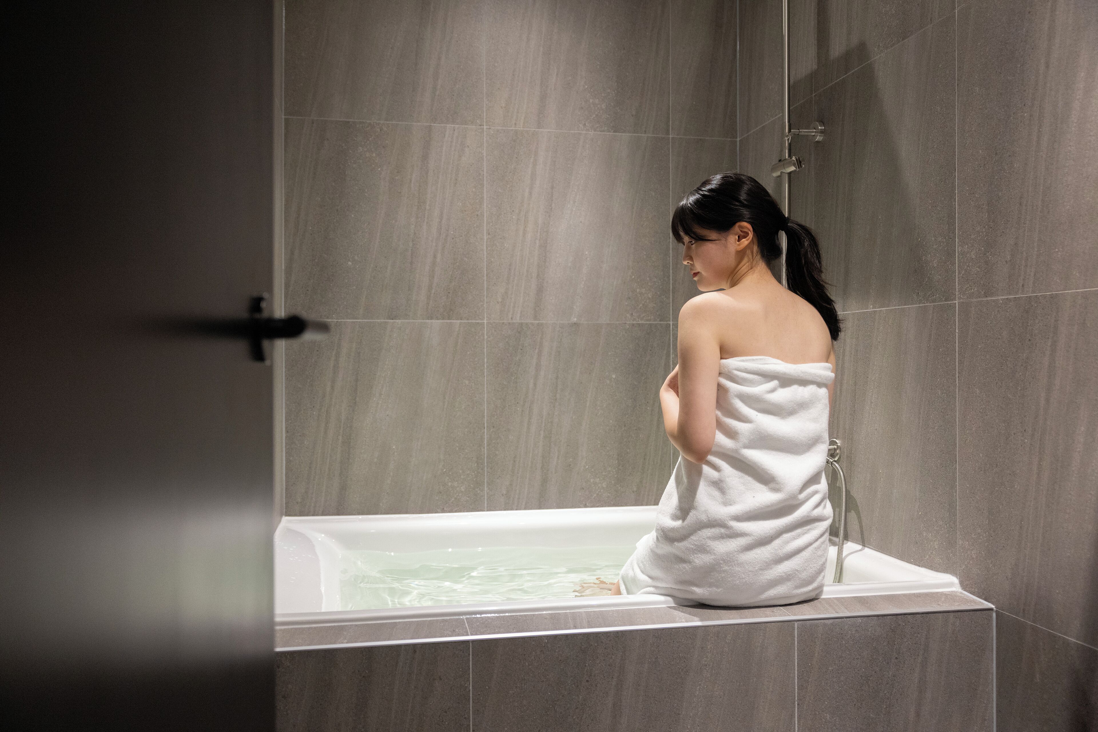 Una persona seduta in una vasca da bagno, in una stanza con pareti piastrellate.