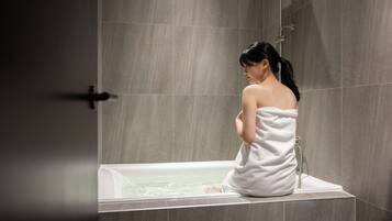 Una persona seduta in una vasca da bagno, in una stanza con pareti piastrellate.