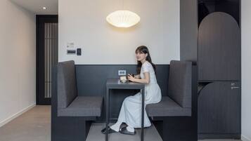 A woman sitting on a bench in a modern room with a table, a light fixture, and a wardrobe.