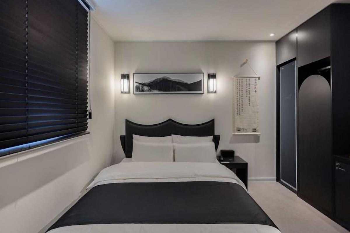 A modern bedroom with a large bed, a headboard, bedside tables, a wall-mounted light, and a door.