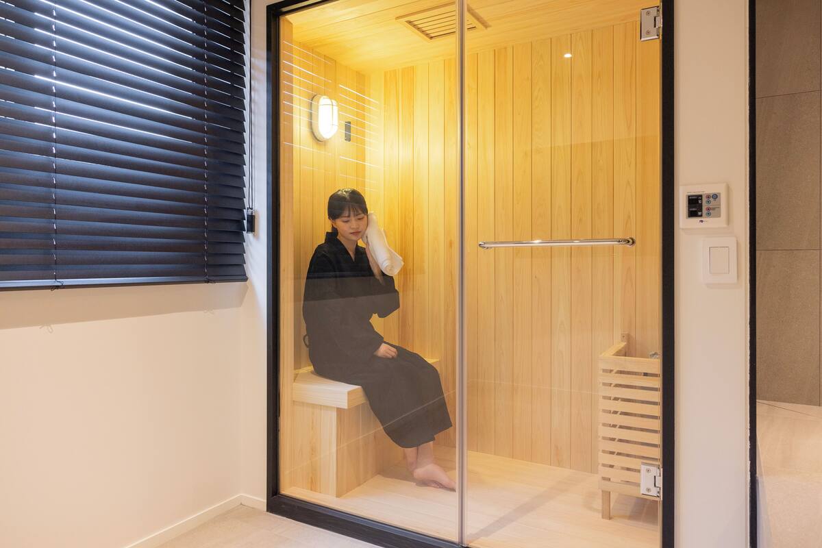 Een sauna met houten wanden en een glazen deur, een bankje, en een bedieningspaneel aan de muur.