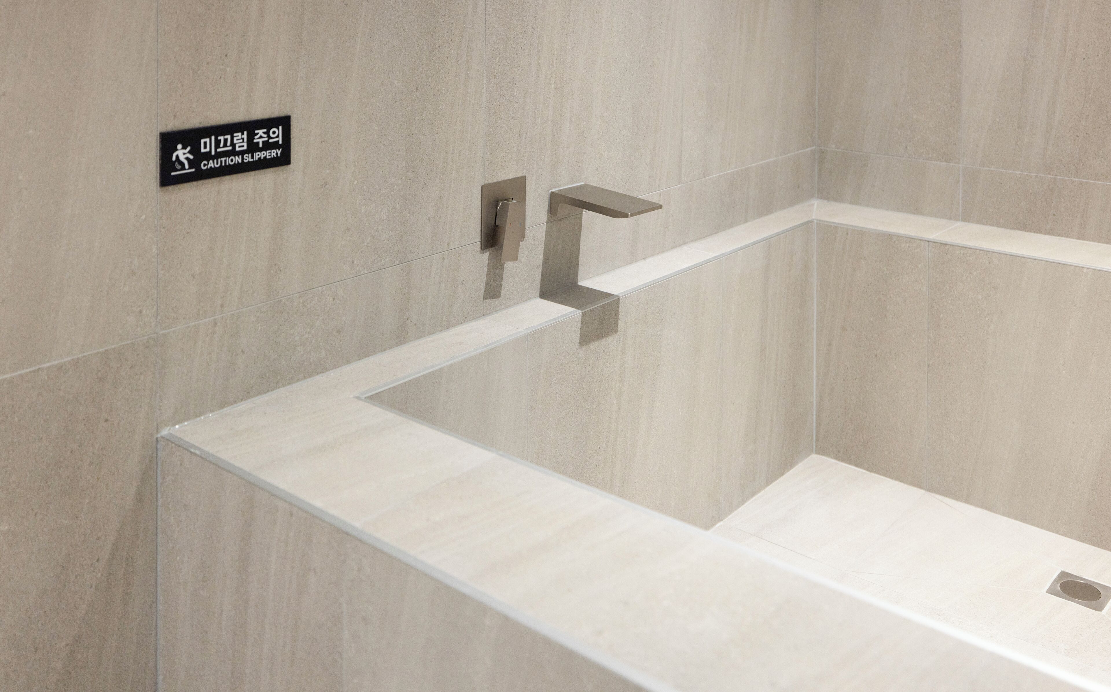 Ein modernes Badezimmer mit einer Rutschgefahr-Warnung, einem eleganten Wasserhahn und einem minimalistischen Design.
