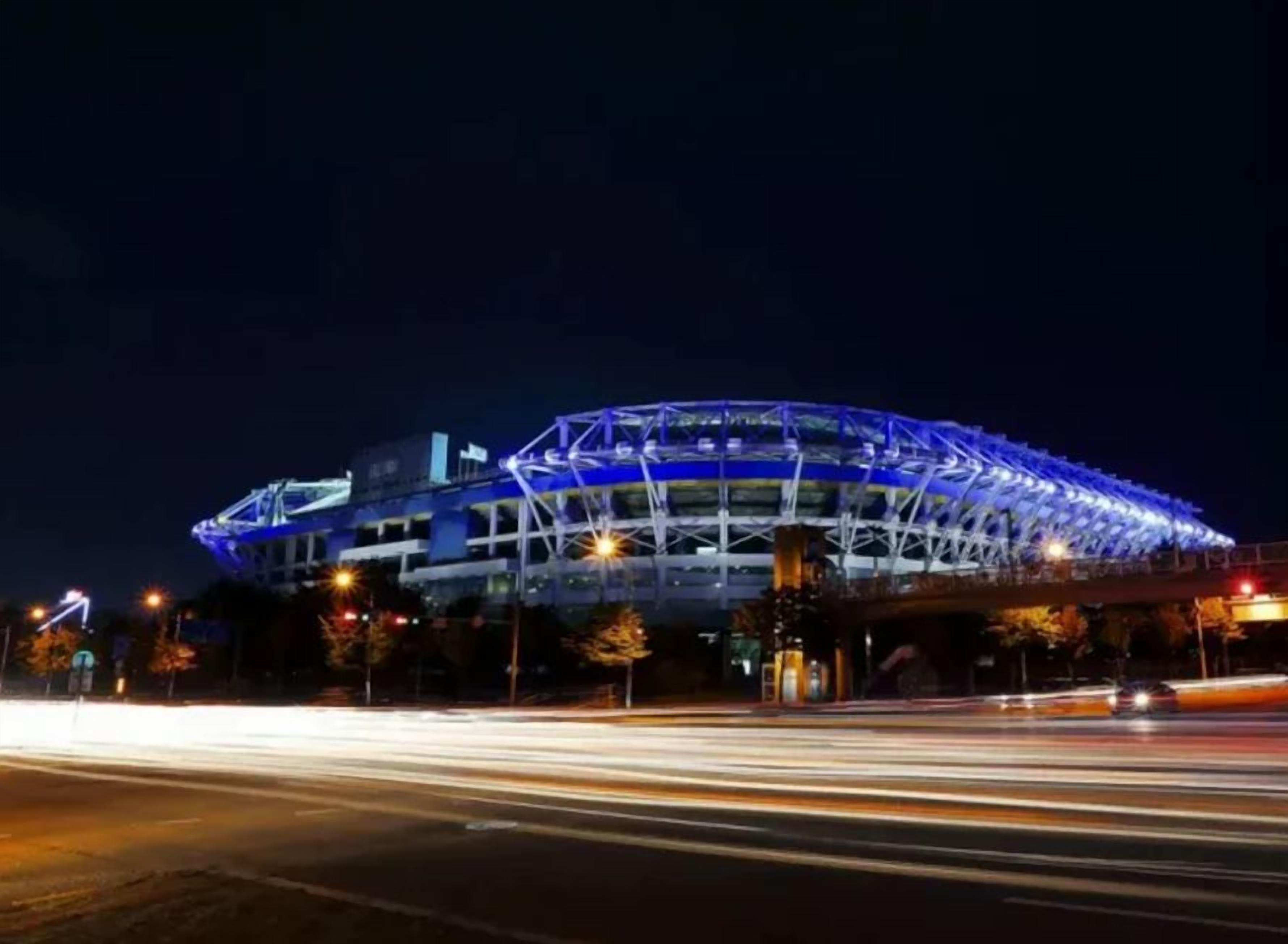 A stadium with a distinctive blue roof structure, surrounded by a well-lit urban environment.