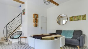 Un salon moderne avec un escalier, un miroir rond, un canapé gris et une chaise blanche.