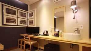 A hotel room with a desk, chair, computer, sink, and framed pictures on the wall. - Busan Deokcheon Den Basta Hotel (Busan)