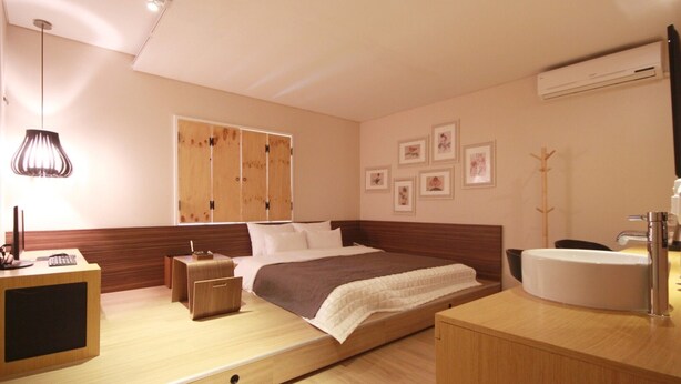 A modern hotel room with a wooden bed, a bedside table with a lamp, a large window, and a bathroom with a sink and mirror. - Busan Deokcheon Den Basta Hotel (Busan)