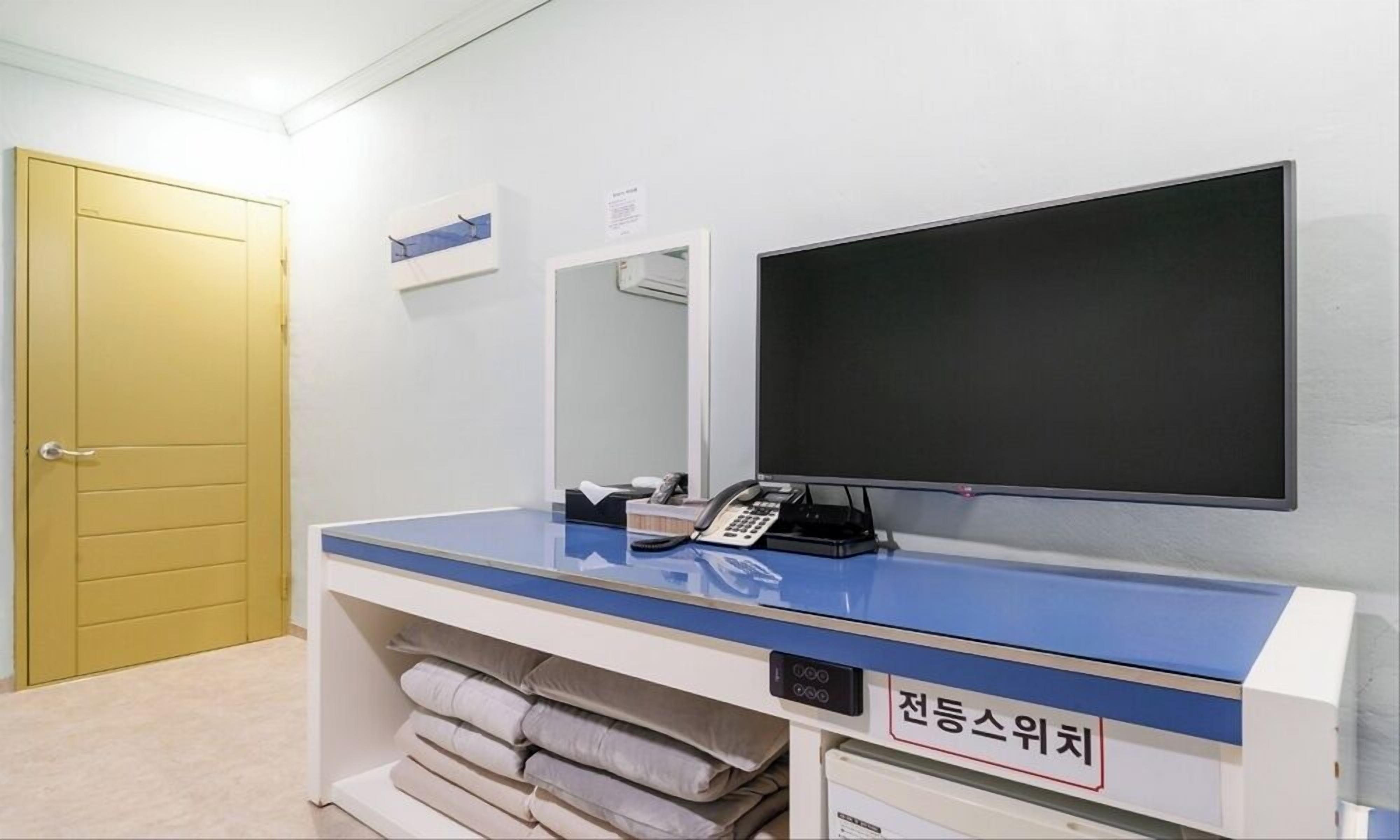 A hotel room with a bed, a desk with a computer, a TV, and a sign indicating a room type.