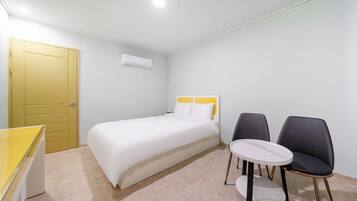 A hotel room with a bed, two chairs, a small table, a yellow door, and an air conditioning unit.