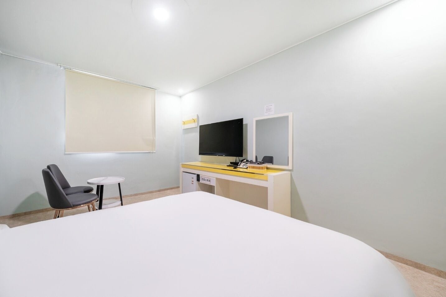 Een hotelkamer met een bed, een bureau met een computer, een stoel, een televisie en een raam met een rolgordijn.