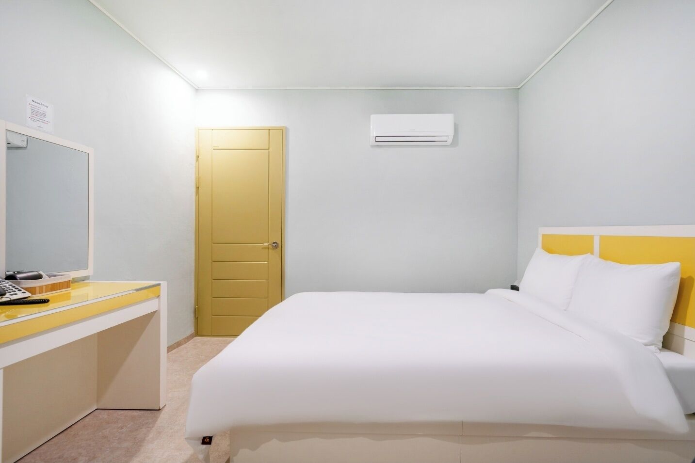 Habitación de hotel con una cama, un escritorio, una silla, una puerta y un equipo de aire acondicionado.