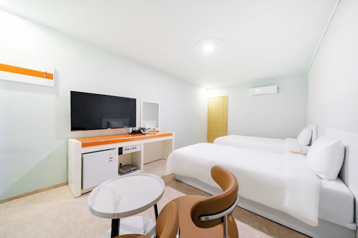 A hotel room with a bed, a desk with a flat-screen TV, a chair, and a small table.