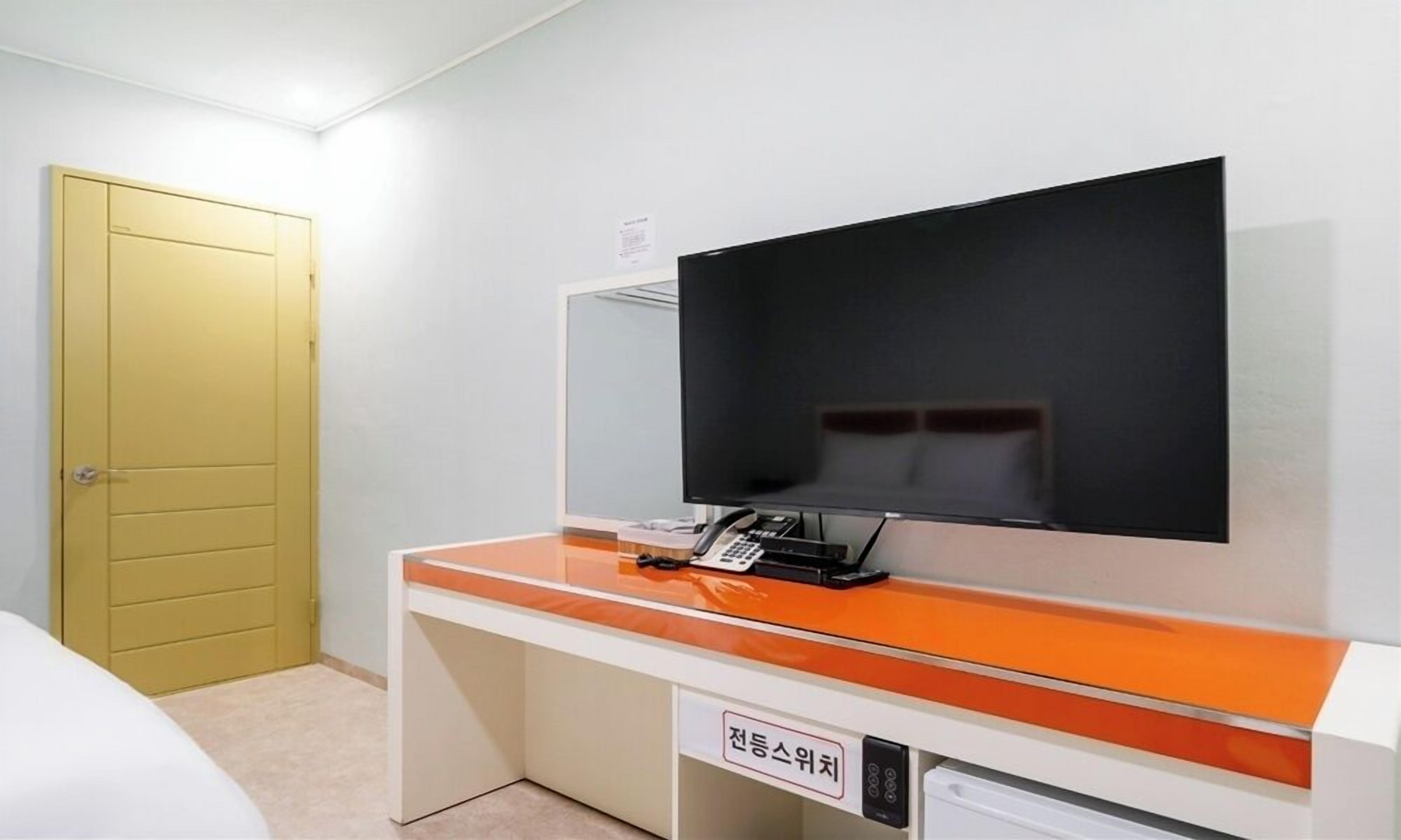 Una camera d'albergo con un letto, una scrivania con il telefono e una televisione a parete.