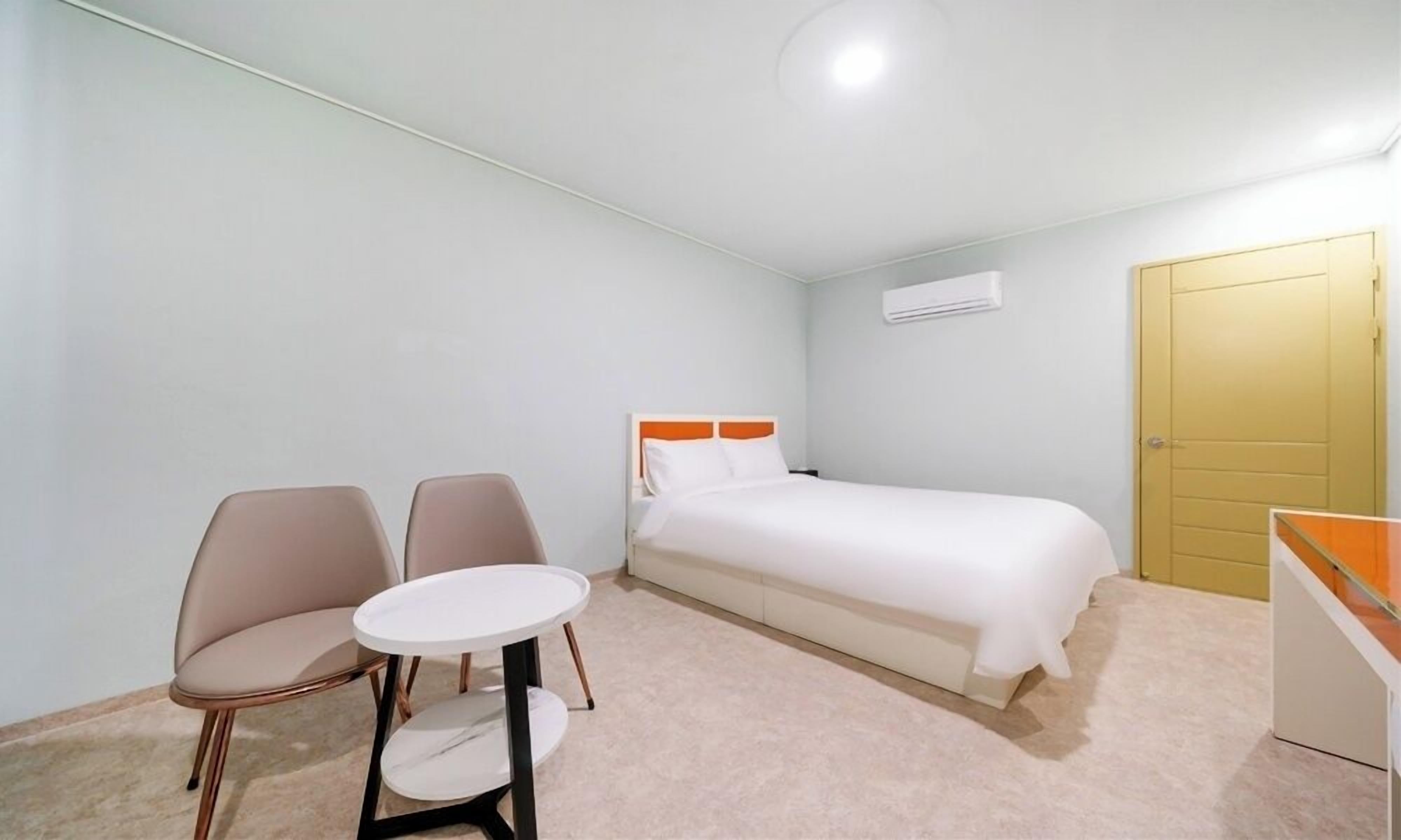 A small, neatly arranged bedroom with a bed, two chairs, a small round table, and a wardrobe.