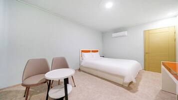 A small, neatly arranged bedroom with a bed, two chairs, a small round table, and a wardrobe.
