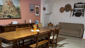 Un comedor con una mesa y sillas de madera, un sofá y una estantería en la pared con objetos decorativos.