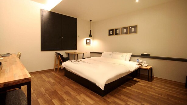 A hotel room with a large bed, a desk with a chair, a small table, and a wardrobe. - Changwon Masan No25 Odong (Changwon)