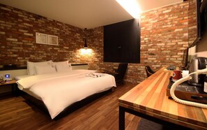 A hotel room with a brick wall, a bed, a desk with a telephone, a coffee maker, and a flat-screen TV. - Changwon Masan No25 Odong (Changwon)