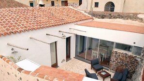 A rooftop patio with a stone wall, a glass door leading to a dining area, and a white awning. - Casa Santa Rughe (Orosei (NU))