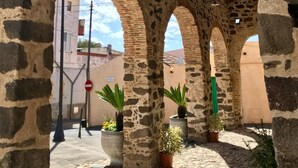 A stone archway with a tiled roof, potted plants, and cobblestone pavement. - Casa Santa Rughe (Orosei (NU))
