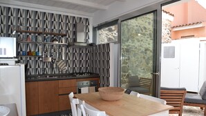A modern kitchen with wooden cabinets, a built-in stove, and a dining area with a wooden table and white chairs. - Casa Santa Rughe (Orosei (NU))