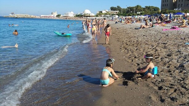 Ein Strand mit Personen, einem Boot und Gebäuden im Hintergrund.
