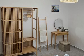 A room with a wooden wardrobe, a ladder, a small table with a mirror, and a picture on the wall.