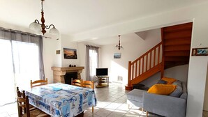 A spacious living area with a dining table, sofa, fireplace, and staircase. - Beachside House with Garden & WiFi, 400m from Shore in Pleumeur-Bodou (Pleumeur-Bodou)