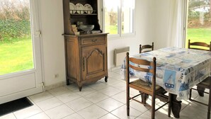 A dining room with a wooden table, chairs, a cabinet with dishes, and a view of the outdoors. - Beachside House with Garden & WiFi, 400m from Shore in Pleumeur-Bodou (Pleumeur-Bodou)