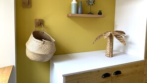Ein Badezimmer mit gelber Wand, einem Holzregal mit Dekoration, einem gewebten Korb und einem Holzkabinett mit Schubladen.