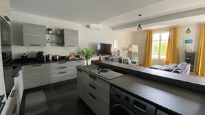 Eine moderne Küche mit integriertem Wasch- und Trockner, einem Essbereich mit gelben Vorhängen und einem großen Fenster, das natürliches Licht hereinlässt.