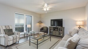 Sala de estar con sofá, sillón, mesa de centro, televisor y balcón con vistas.