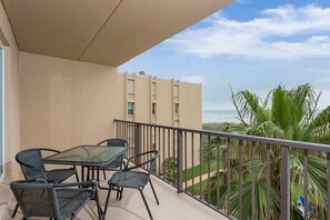 Un balcon avec une table et des chaises, donnant sur une plage et des palmiers.