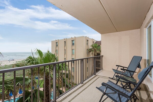 Un balcon avec vue sur la plage et l’océan, équipé de deux chaises longues et d’un petit espace piscine.