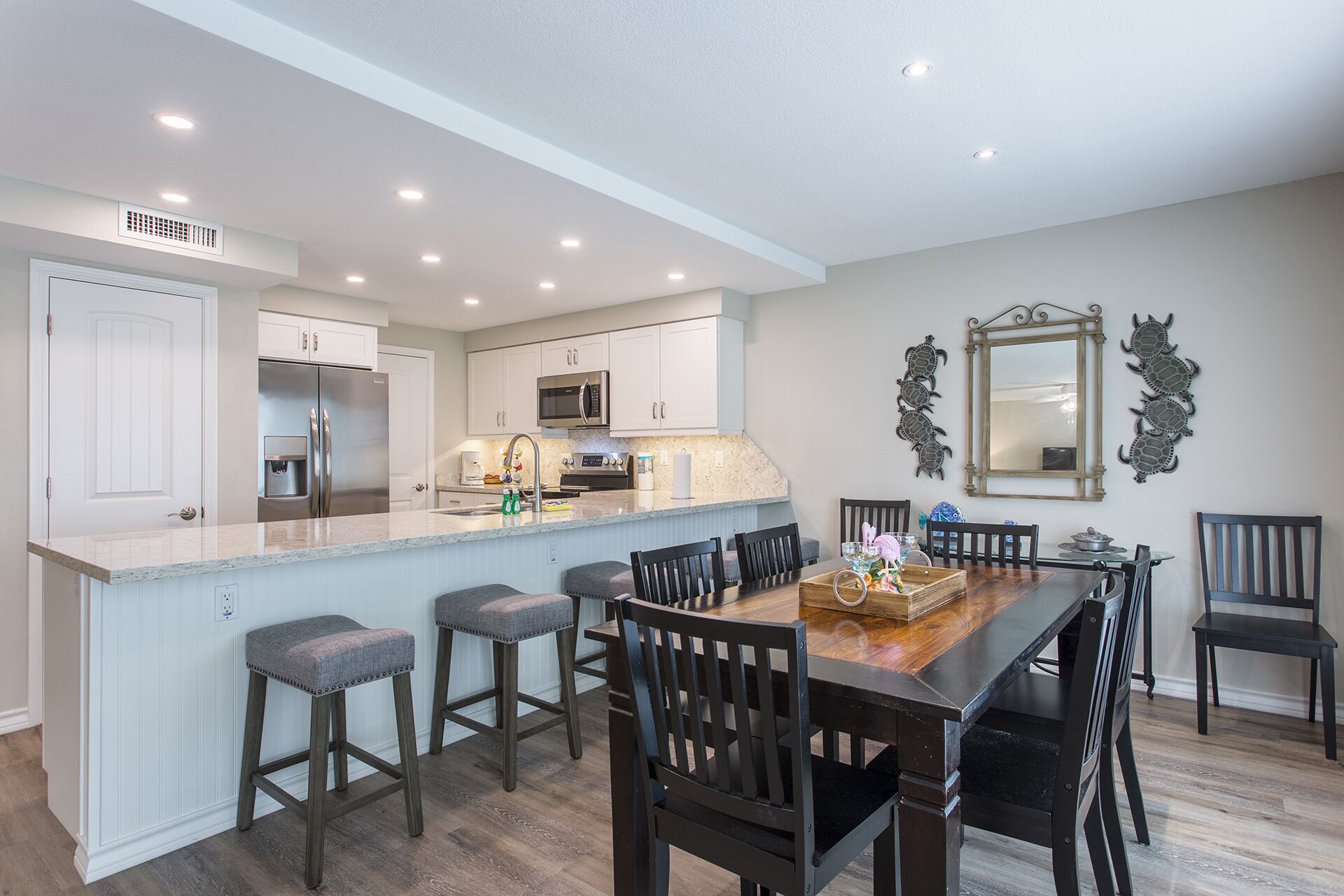 A modern kitchen with white cabinets, a stainless steel refrigerator, and a central island with bar stools.