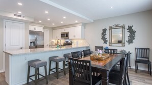Una cocina moderna con armarios blancos, un refrigerador de acero inoxidable y una isla central con taburetes de bar.