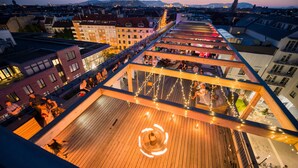 Una terraza en la azotea con piso de madera, zonas de estar y luces colgantes.