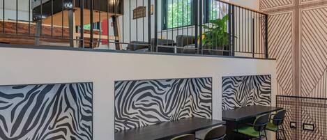 A modern interior with a staircase, zebra-patterned walls, and a dining area with black tables and green chairs.
