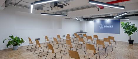 A conference room with rows of chairs, a projector screen, and a potted plant.