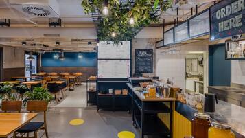 Um café moderno com mesas, cadeiras, um quadro de cardápio e um balcão com a placa que diz 'ORDER HERE'.