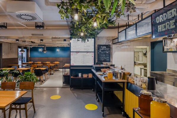 A modern cafe with tables, chairs, a menu board, and a counter with a sign that says "ORDER HERE".