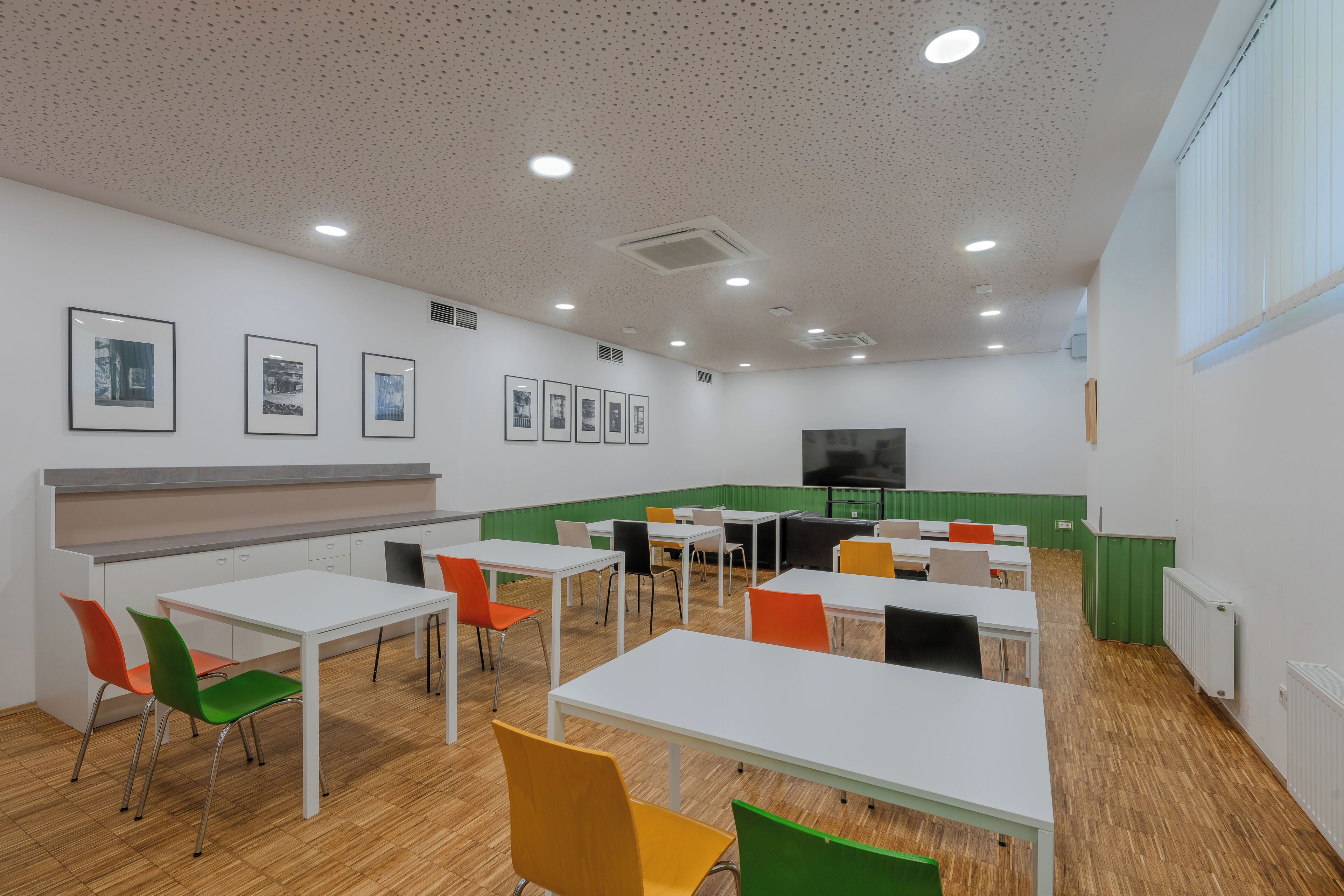 Un comedor moderno con mesas y sillas blancas, un muro verde decorativo y cuadros en la pared.