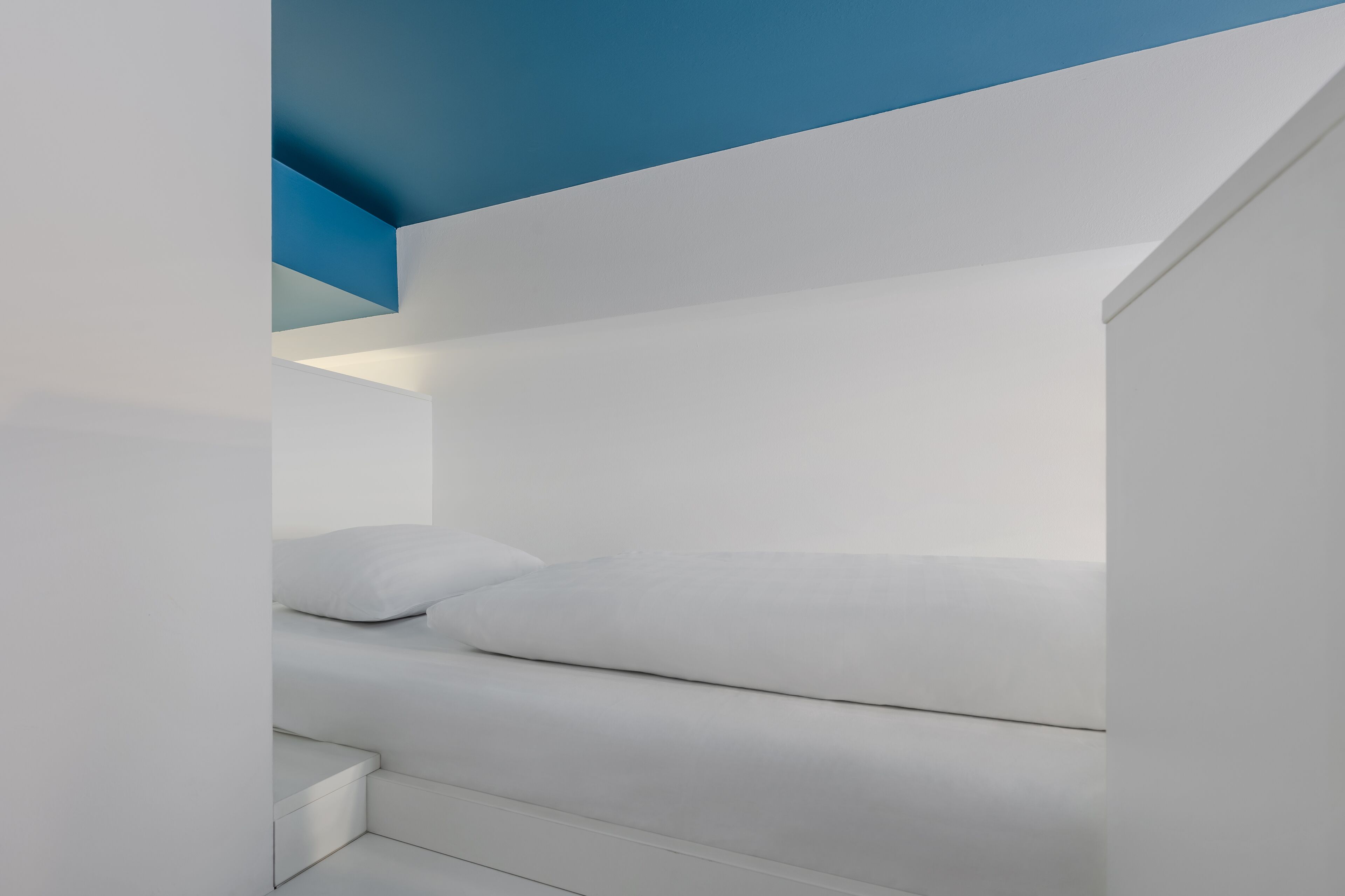 Une chambre moderne et minimaliste, avec un lit blanc et un mur d’accent bleu.
