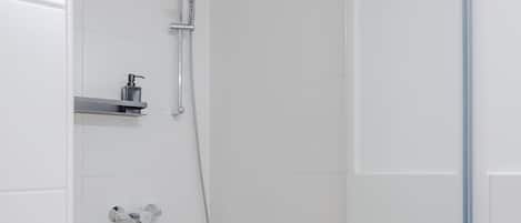 Un espacio de ducha pequeño y cerrado, con un cabezal de ducha manual, un grifo de pared y un estante con dispensador de jabón.