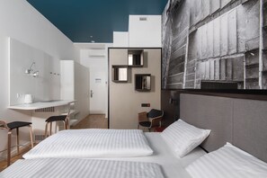 Quarto de hotel moderno com cama, duas cadeiras, escrivaninha e uma grande obra de arte na parede.