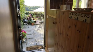 Eine Holztür, die auf eine Terrasse mit Grill, Blumentöpfen und Gartenmöbeln führt.