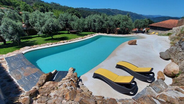 A swimming pool with a stone border, two yellow lounge chairs, and a view of a mountainous landscape. - For families who love nature and the countryside. (Celorico de Basto)